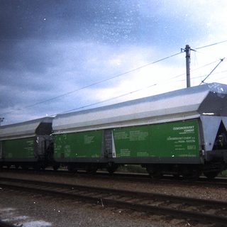 Green flatcar train cars on tracks under cloudy sky.