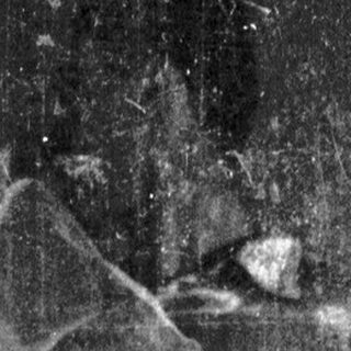 Here's a brief summary of the image: Figure in draped fabric, obscured in dark, textured monochrome.