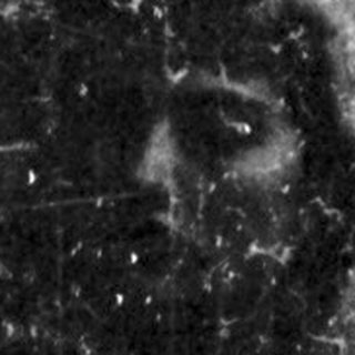 Man kneeling, head bowed, in a dark, textured space.