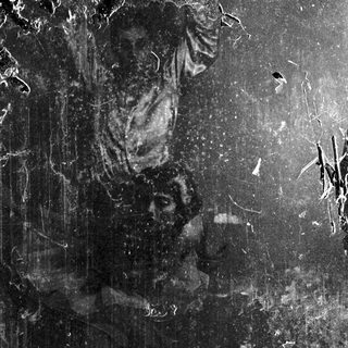 Man kneeling, head bowed, in a dark, textured space.