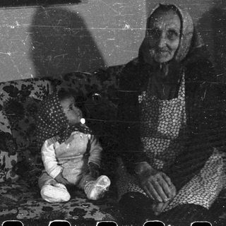 Elderly woman sits with a child on a floral sofa.