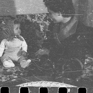 Baby sits on a patterned couch, being watched.