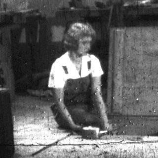Worker sits on floor in a cluttered, industrial-like space.