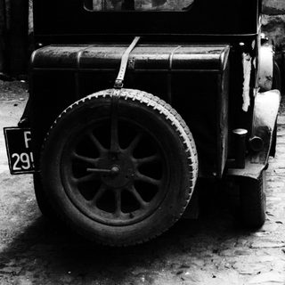 Vintage car's rear tire and license plate in black and white.