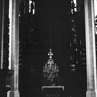 Here's a brief summary of the image: Dark interior of a church with a chandelier.
