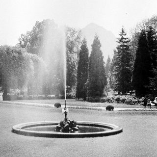 Fountain in a garden with trees and a mountain backdrop.