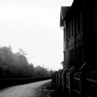 Building alongside a road, bordered by trees and fence.