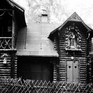 Log cabin with statue and fence, in black and white.