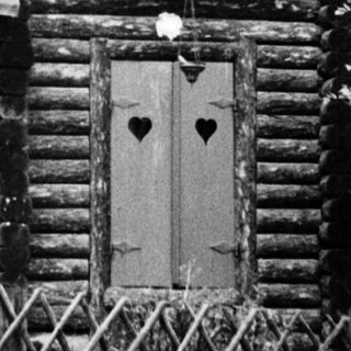 Log cabin with statue and fence, in black and white.