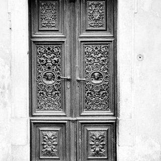Here's a brief summary of the image: Ornate, antique wooden doors set into a stone wall.