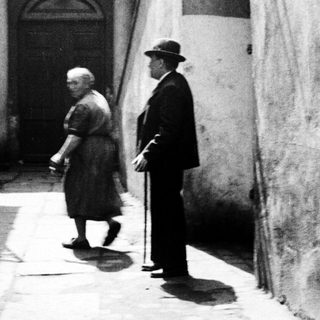 Here's a brief summary of the image: Older couple walking along a narrow, stone-paved alleyway.
