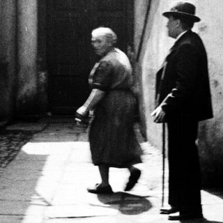 Here's a brief summary of the image: Older couple walking along a narrow, stone-paved alleyway.