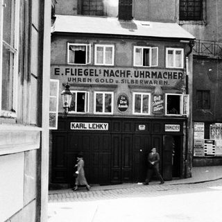 Black and white photo shows a storefront and passersby.