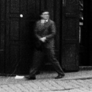 Black and white photo shows a storefront and passersby.