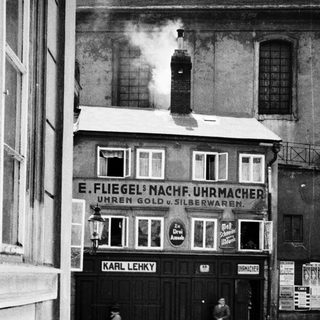 Black and white photo shows a storefront and passersby.