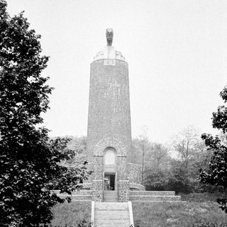 People walking toward a monument with a statue on top.