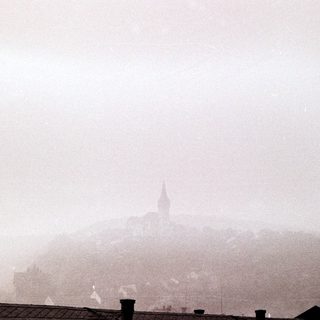 Misty, monochrome cityscape with a distant church spire.