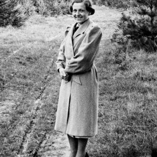 Woman in a coat stands on a dirt road.