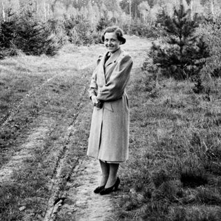 Woman in a coat stands on a dirt road.