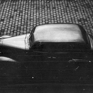 Vintage car sits parked on a cobblestone street.