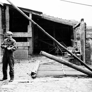 Man stands in a dilapidated yard with fallen lumber.