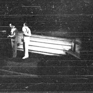 Here's a brief summary of the image: Three figures near a boat at night.