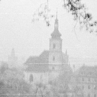 Misty landscape featuring a church and silhouetted tree branches.