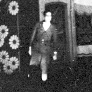 Here's a brief summary of the image: Person stands near a building with an arched doorway.