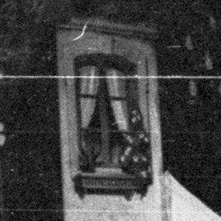 Here's a brief summary of the image: A person stands near a building with an arched doorway.