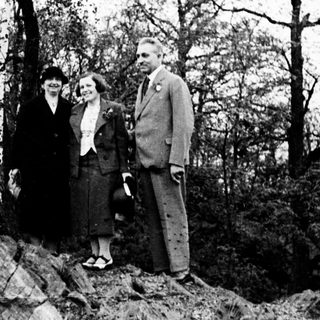 Couple stands on rocky hillside in vintage clothing.
