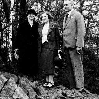 Couple stands on rocky hillside in vintage clothing.