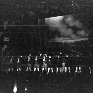 Group of men stand near a building, smoke visible.