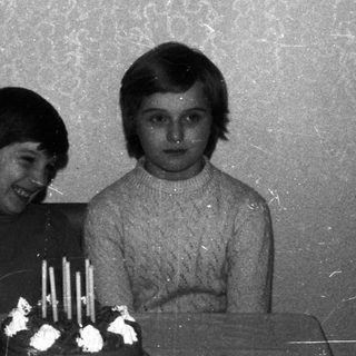 Three children stand near a birthday cake.