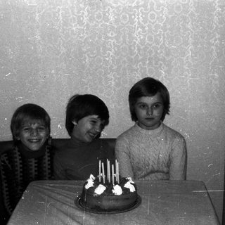 Three children stand near a birthday cake.