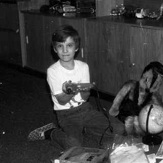 Boy sits with toy airplane and stuffed animal indoors.