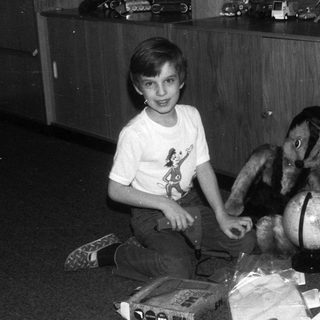 Boy sitting with a stuffed animal and toys.