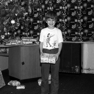 Boy stands near a Christmas tree holding a wrapped gift.