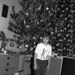 Boy stands near a Christmas tree with presents.