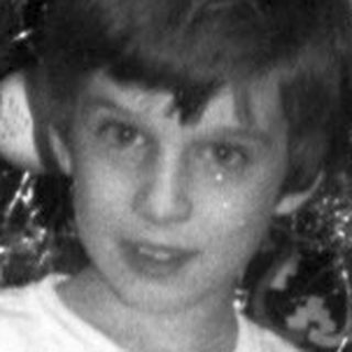 Boy stands near a Christmas tree with presents.
