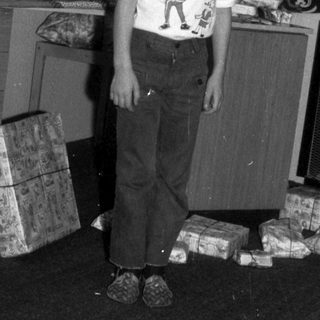 Boy stands near a Christmas tree with presents.