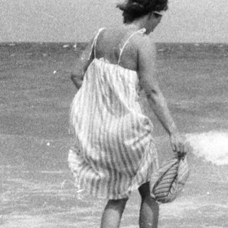 Boy sits in a hole on a beach, woman in background.