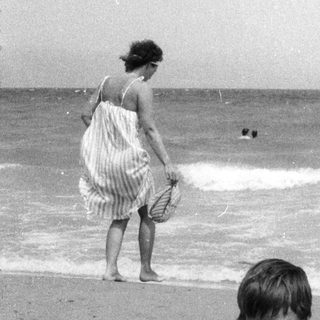 Boy sits in a hole on a beach, woman in background.