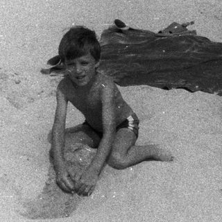 Two boys relax on a beach, one playing in the sand.