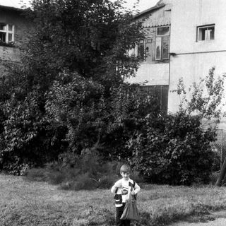 Boy stands on a cobblestone street near a building.