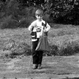 Boy stands on a cobblestone street near a building.