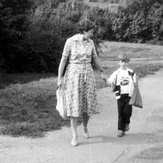 Woman and child walk along a road, viewed from behind.