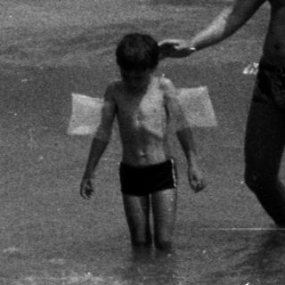 Man and child walk in ocean waves on a beach.