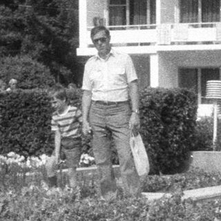Man and boy stand near tiered garden in front of building.