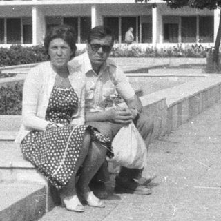People seated on a ledge, building and landscaping in background.