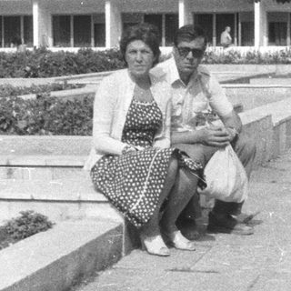 People seated on a ledge, building and landscaping in background.